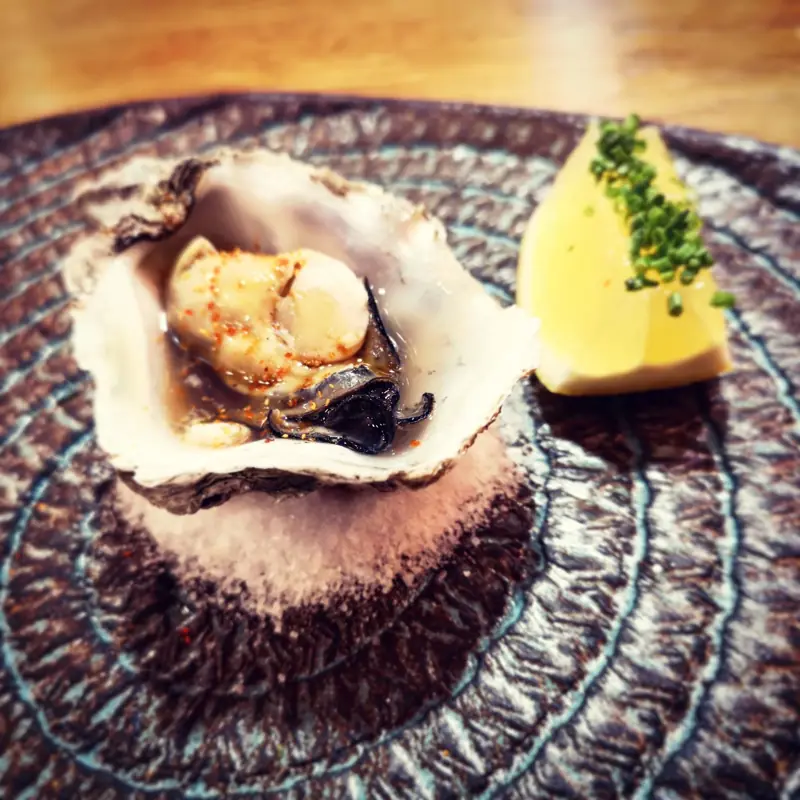 A grilled oyster in its shell with a wedge of lemon